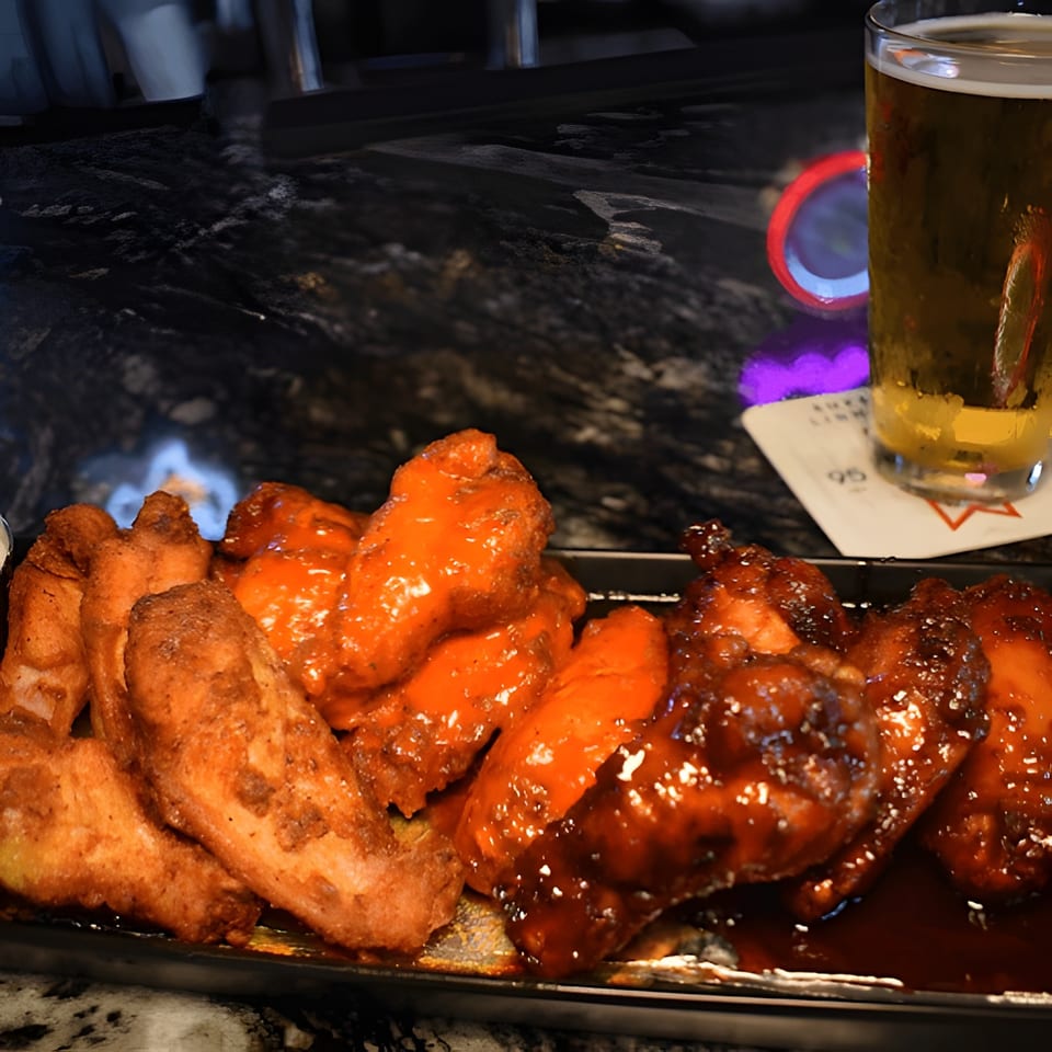 A platter of buffalo wings, some spicy orange and some BBQ brown, with a beer.