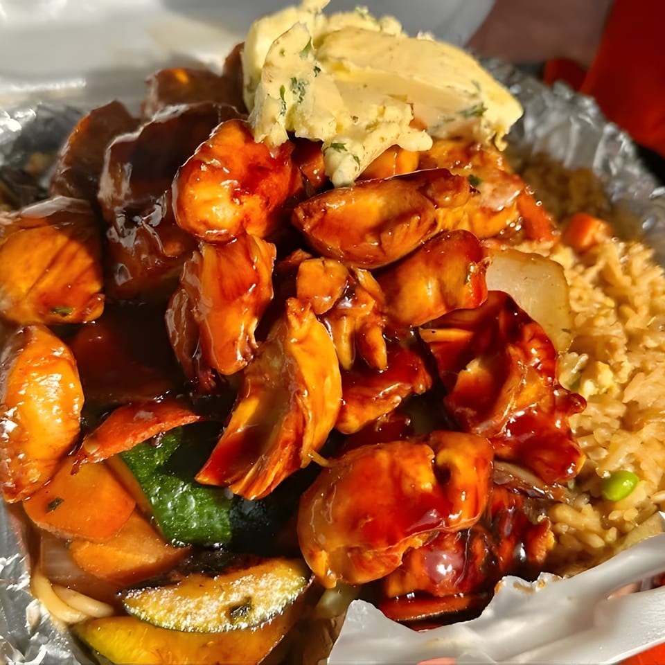 Teriyaki chicken, fried rice, mixed vegetables, and mashed potatoes in a takeout container.