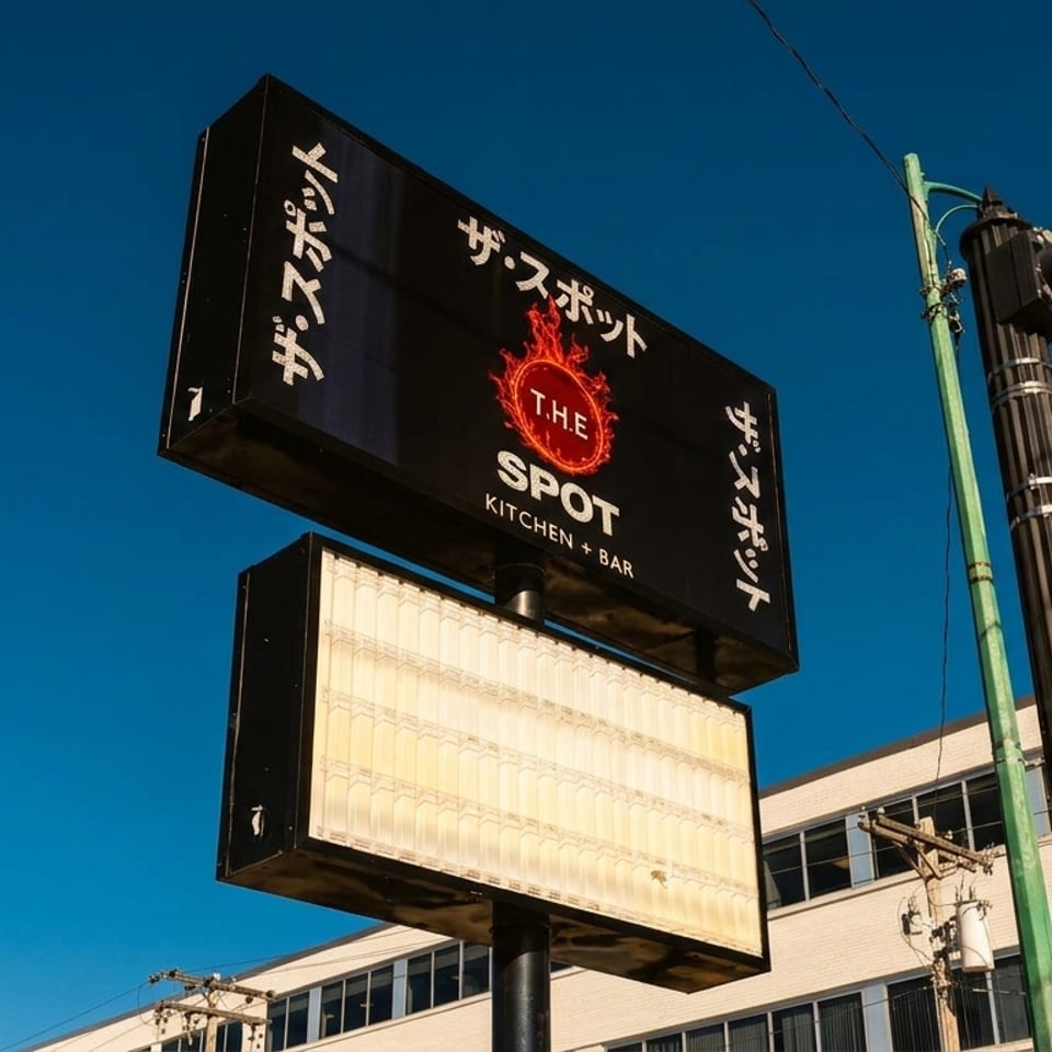 A black sign for "The Spot Kitchen + Bar" with a fiery logo against a clear blue sky.