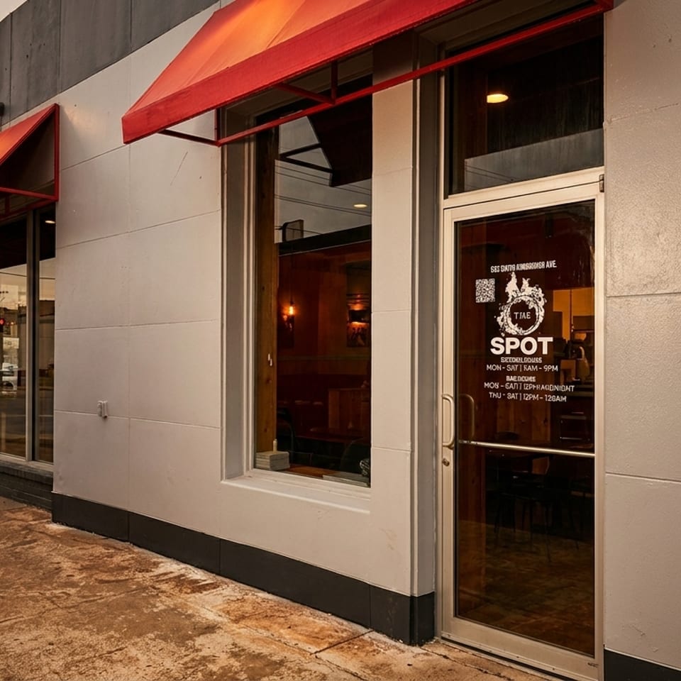 Exterior of The Spot restaurant with red awnings, large windows, and a door displaying hours.